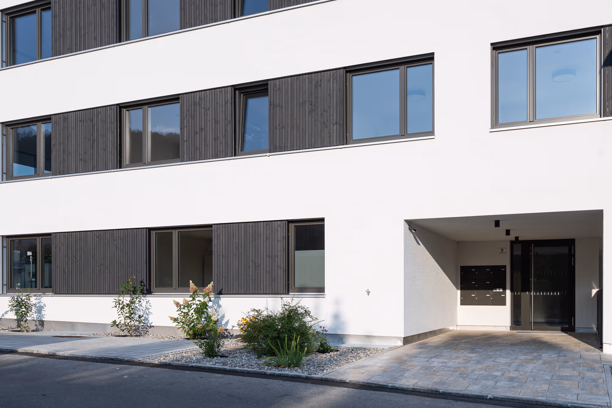 Fassade von Field Lane 9 in Götzis mit schwarzen Fensterrahmen und Vorgarten.
