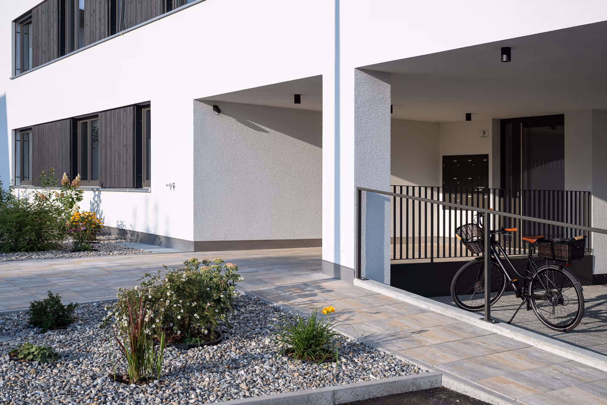 Hauseingang von Field Lane 9 in Götzis mit Bepflanzung und Fahrradabstellplatz.