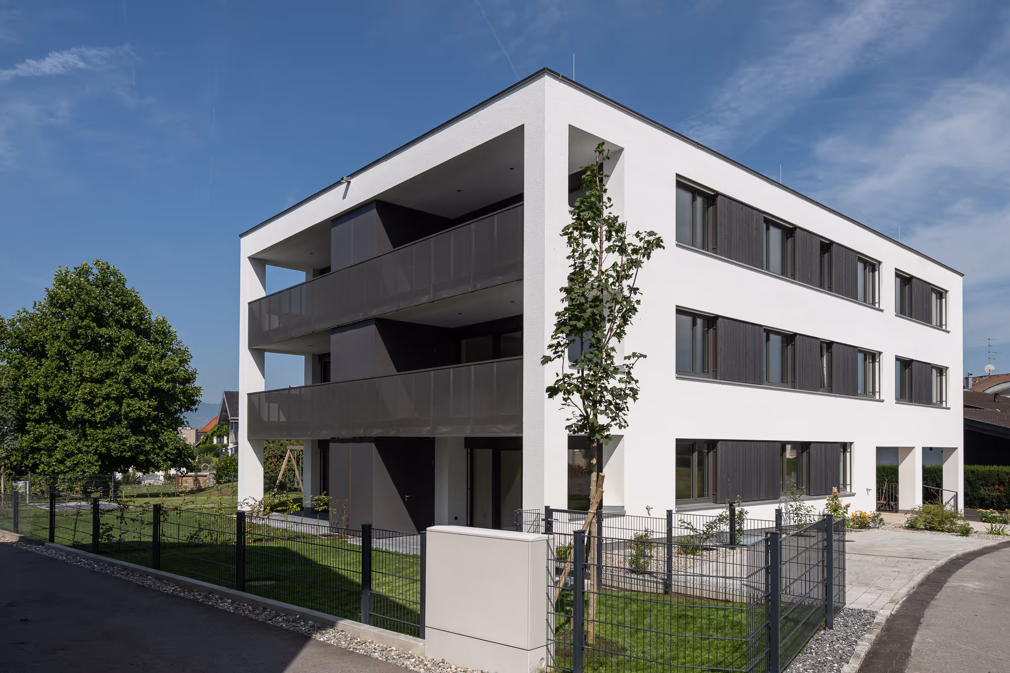Field Lane 9 in Götzis: dreigeschossiges Wohnhaus mit dunklen Balkongeländern.